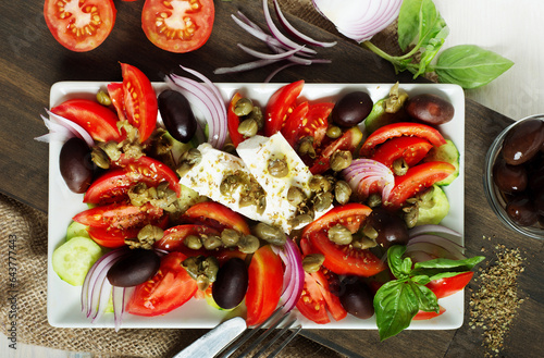 Classic Greek salad of tomatoes, olives, red onions, cucumbers and capers on a rectangular plate
