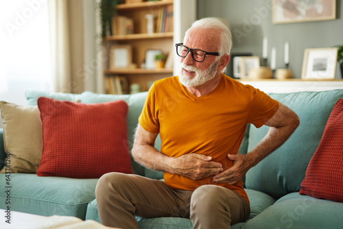 Schilderij op canvas Senior man suffering from stomach ache sitting on a couch in the living room at