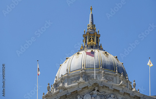 San Francisco, CA, USA - July 12, 2023: Gray stone City Hall giant dome under blue sky. Golden decorations at and on spire. 3 Flags on top: country, state, city photo