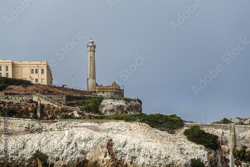 San Francisco, CA, USA - July 12, 2023: Alcatraz Island SW tip with lighthouse closeup. White guano covered rocky cliffs with sparse green bushes under light blue sky. Main building part