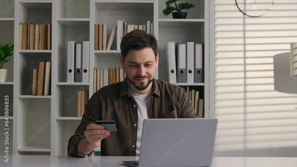 Smiling satisfied male client Caucasian man businessman worker at home office use laptop pay money online with bank credit card internet easy financial app business shopping e-commerce order web store Smiling satisfied male client Caucasian man businessman worker at home office use laptop pay money online with bank credit card internet easy financial app business shopping e-commerce order web store