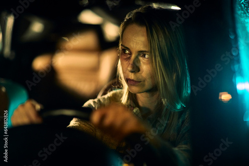 A young Caucasian woman, bearing the painful signs of domestic abuse with visible bruises and blackened eyes, drives her car at night photo