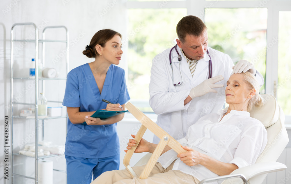 Obraz premium Man dermatologist examining female face skin. Mature woman getting professional help during appointment visit to expert in cosmetology and dermatology, female assistant write recommendations for care