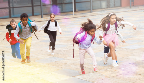 Team of positive schoolchildren running in race in the street and laughing outdoors