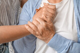 Young woman with her grandmother holding hands at home, closeup