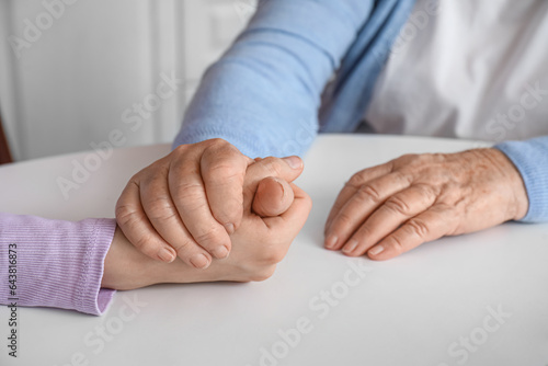 Young woman with her grandmother holding hands at table in kitchen  closeup