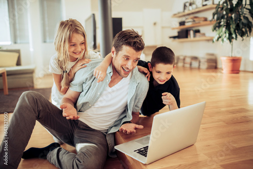 Young dad using the laptop with his kids in the living room at home