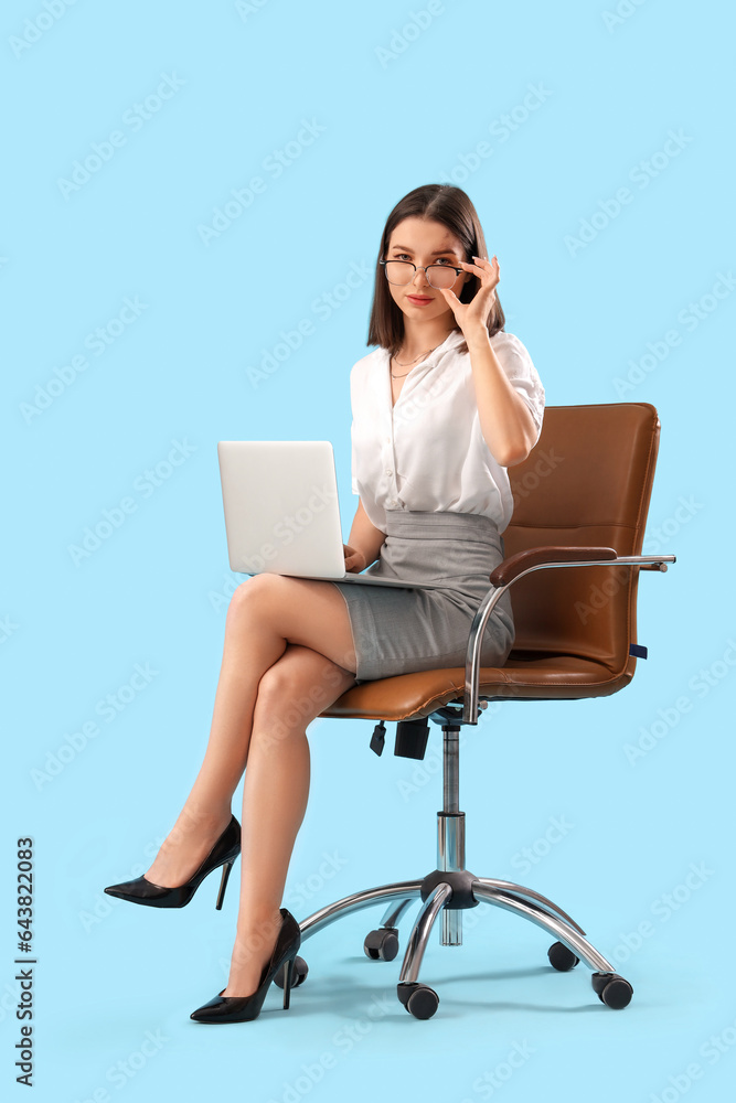 Young businesswoman with laptop sitting in chair on blue background Young businesswoman with laptop sitting in chair on blue background
