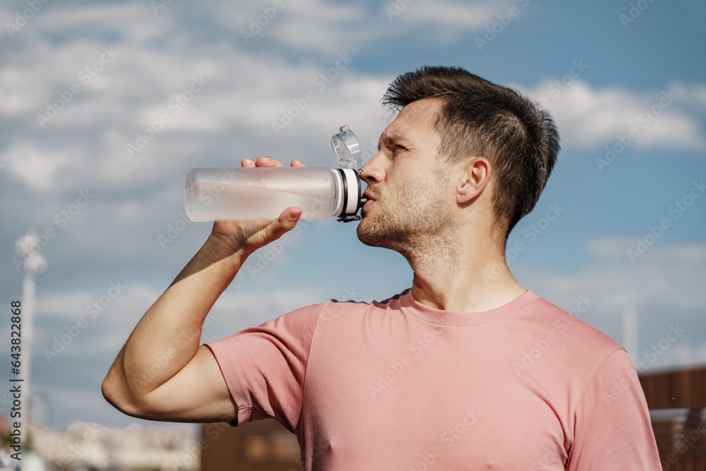 A man drinks water from a sports bottle. The athlete is a confident