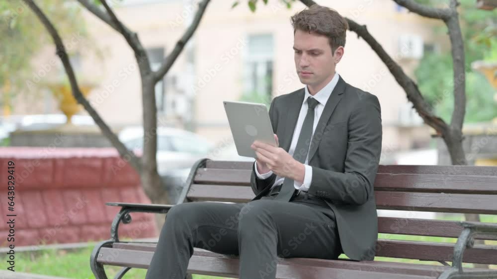 Businessman using Tablet while Sitting on Bench Businessman using Tablet while Sitting on Bench