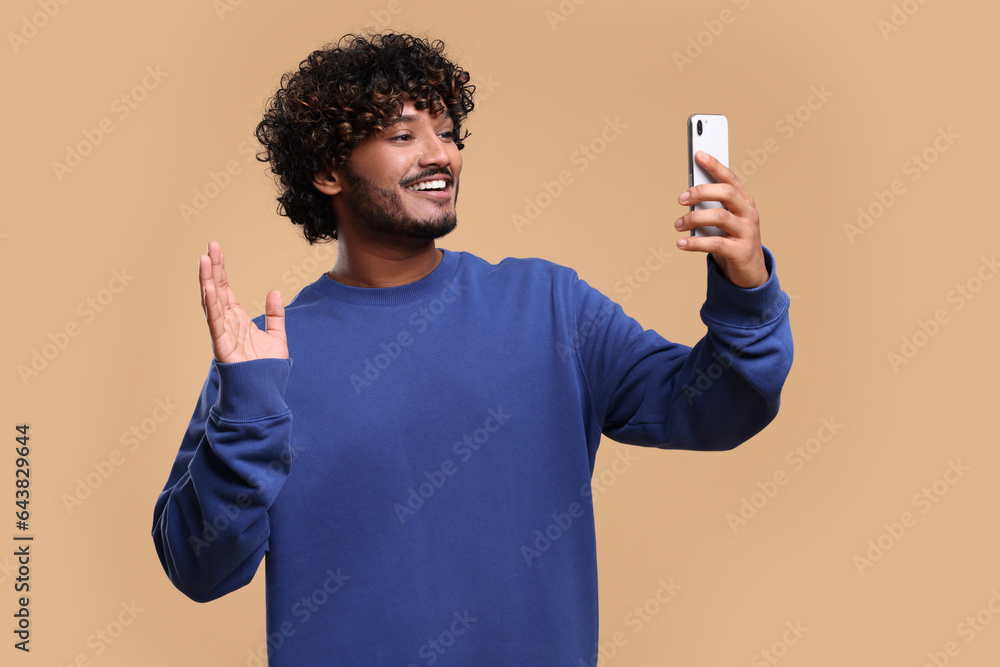 Handsome smiling man having video call via smartphone on beige background Handsome smiling man having video call via smartphone on beige background