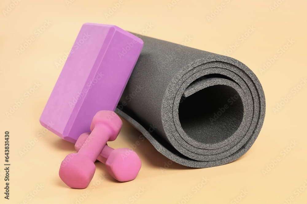 Grey exercise mat, yoga block and dumbbells on beige background Grey exercise mat, yoga block and dumbbells on beige background