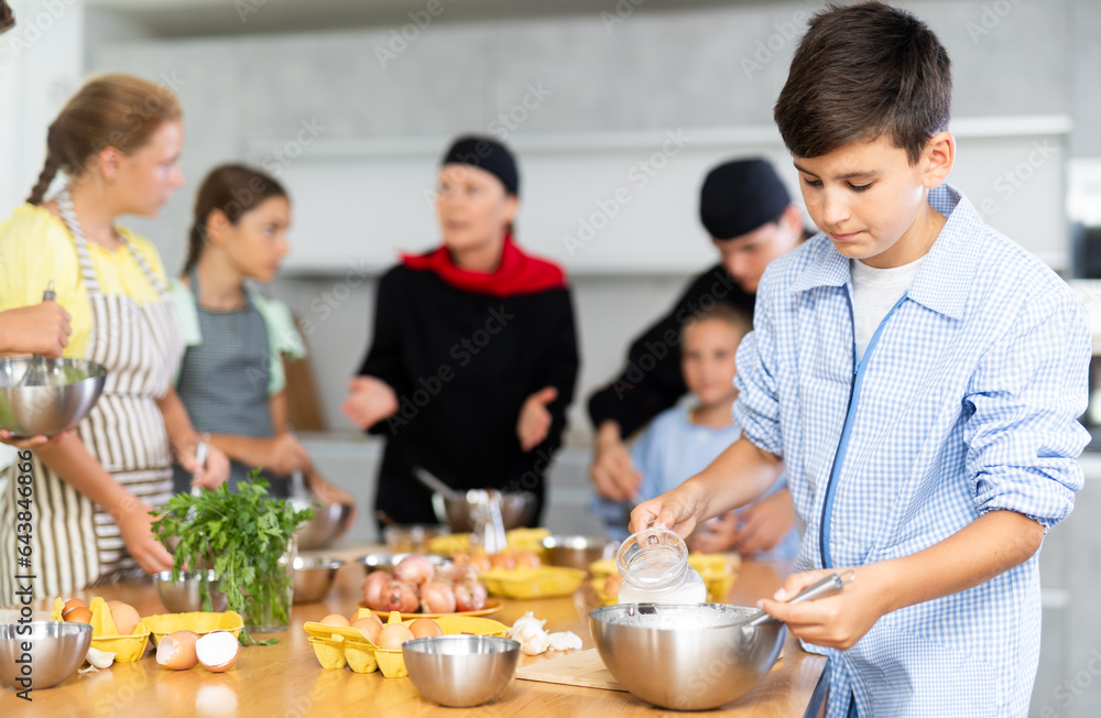 Curious teen boy participating in culinary workshop led by professional chefs for tweens and learning how to cook..