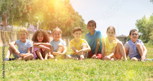 Group of happy kids friends resting on grass together in park at summer day