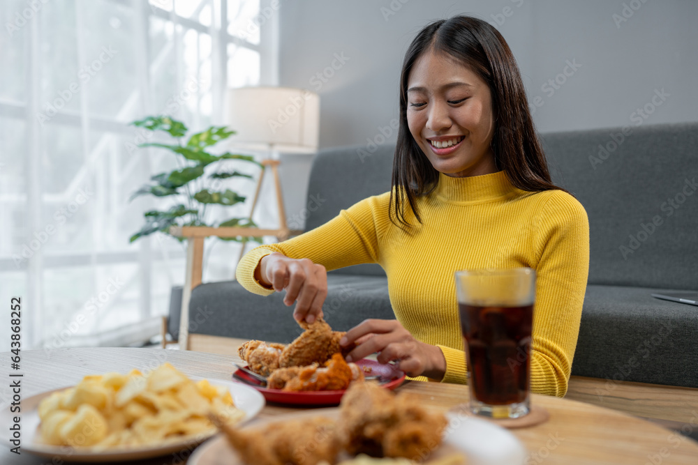 Happy Asian young woman eating delicious crispy fried chicken in the living room at home. family party Smile, laugh, enjoy food and drink, lifestyle concept, celebrate holidays. Happy Asian young woman eating delicious crispy fried chicken in the living room at home. family party Smile, laugh, enjoy food and drink, lifestyle concept, celebrate holidays.