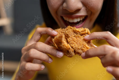 Foto Happy Asian young woman eating delicious crispy fried chicken in the living room at home
