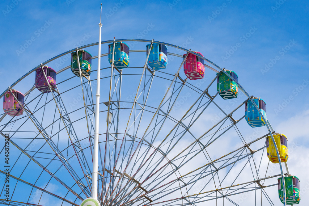  a photo of a rainbow ferris wheel that stands out against a blue sky with white clouds.