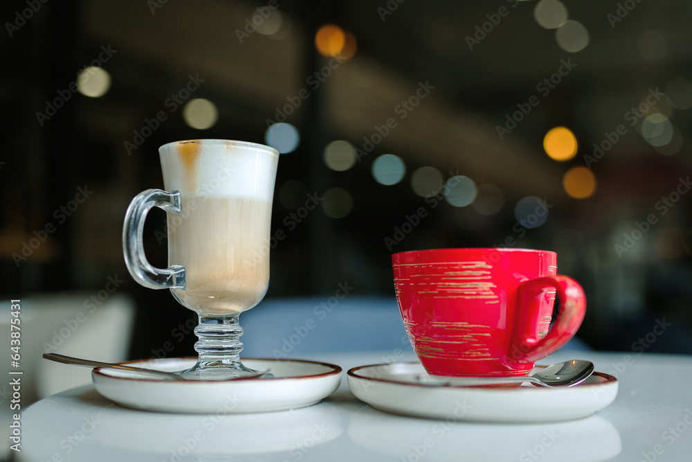 Fototapeta premium A cup of latte coffee and a cup of tea on a table in a coffee shop, the eternal dispute of tea or coffee.