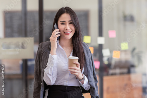 Portrait of young asian woman, company worker in phone smiling and call phone, standing over white background