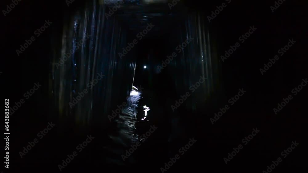 Digger person walking through dark tunnel adit, rain collector, sewer tunnel underground, illuminating light of lantern flashlight. Infrastructure of mine adit for underground river. Sewage collector Digger person walking through dark tunnel adit, rain collector, sewer tunnel underground, illuminating light of lantern flashlight. Infrastructure of mine adit for underground river. Sewage collector