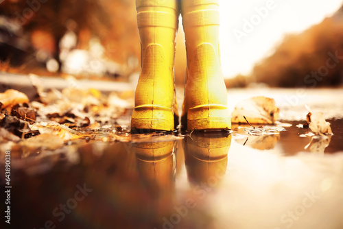 Kid standing on foliage . Legs of children in  boots standing in puddle with orange fallen leaves in autumn.