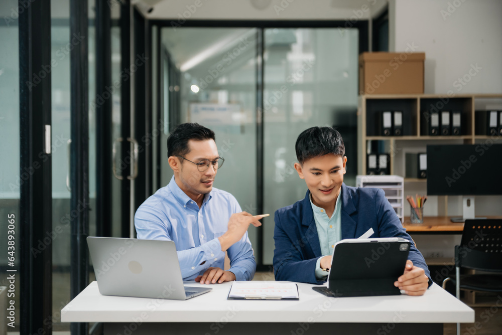 Two Asian businessman discuss investment project working and planning strategy with tablet laptop computer in modern office. Two Asian businessman discuss investment project working and planning strategy with tablet laptop computer in modern office.
