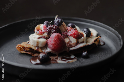 Delicious sweet wheat flour crepe, with cajeta and red berries, on a black plate, dark food, homemade, healthy breakfast