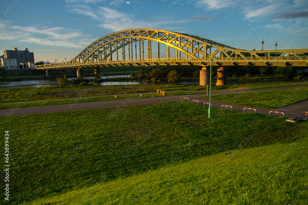Fototapeta premium Asahibashi bridge cross over the Ishikari river with outdoor park on the riverbank, Asahikawa, Kamikawa Subprefecture, Hokkaido, Japan