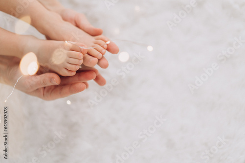 Children s bare feet in the hands of an adult in the lights of garland