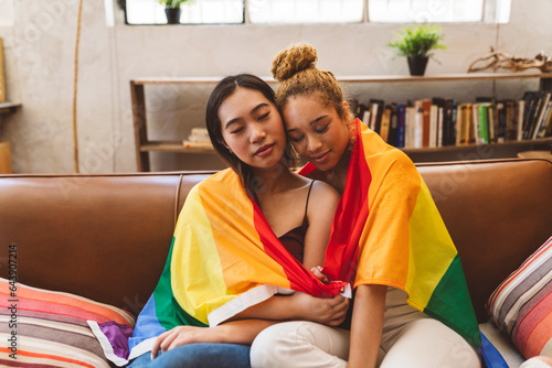 two young multiracial lesbian women at home gay pride flag love
