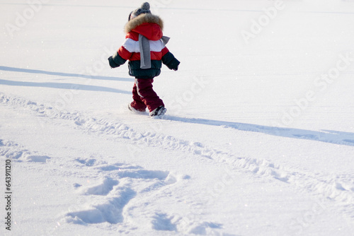 Funny little child runs in the snow. Boy playing in big snow in winter. Happy caucasian child playing in snow