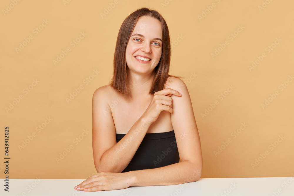 Cute adorable young happy woman wearing black top looking at camera posing isolated over beige background expressing happiness smiling with joyful face. Cute adorable young happy woman wearing black top looking at camera posing isolated over beige background expressing happiness smiling with joyful face.