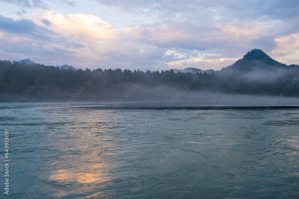 A wide, full-flowing mountain river with a fast current at dawn or sunset. Mountains and forest in the fog. A large turquoise-colored mountain river Katun in the Altai Mountains, Altai Republic.