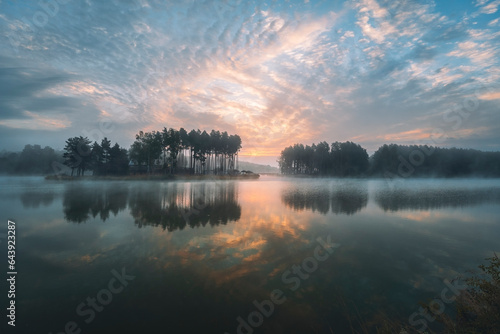 Sunrise over the lagoon. Misty summer morning. Pine trees on the other shore. Krasnobrod, Roztocze, Poland