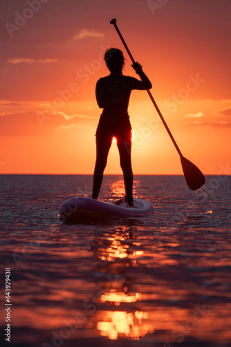 SUP. Stand up shovel. Adventurous girl on the paddle board rows during a bright and vibrant sunset.Silhouette of woman paddleboarding at sunset. Canakkale, Türkiye.