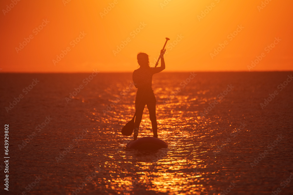 SUP. Stand up shovel. Adventurous girl on the paddle board rows during a bright and vibrant sunset.Silhouette of woman paddleboarding at sunset. Canakkale, Türkiye.