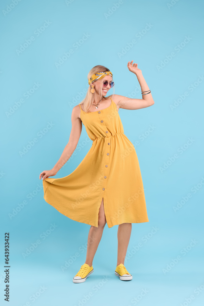 Portrait of smiling hippie woman dancing on light blue background