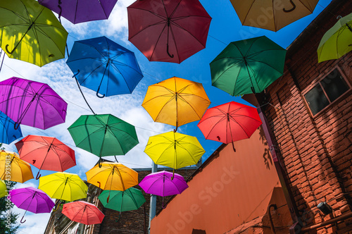 Colorful streets. Colorful umbrellas suspended from above on the street near the houses. Decoration near houses made of umbrellas. Joyful atmosphere on the streets. Rainbow colors on umbrellas.