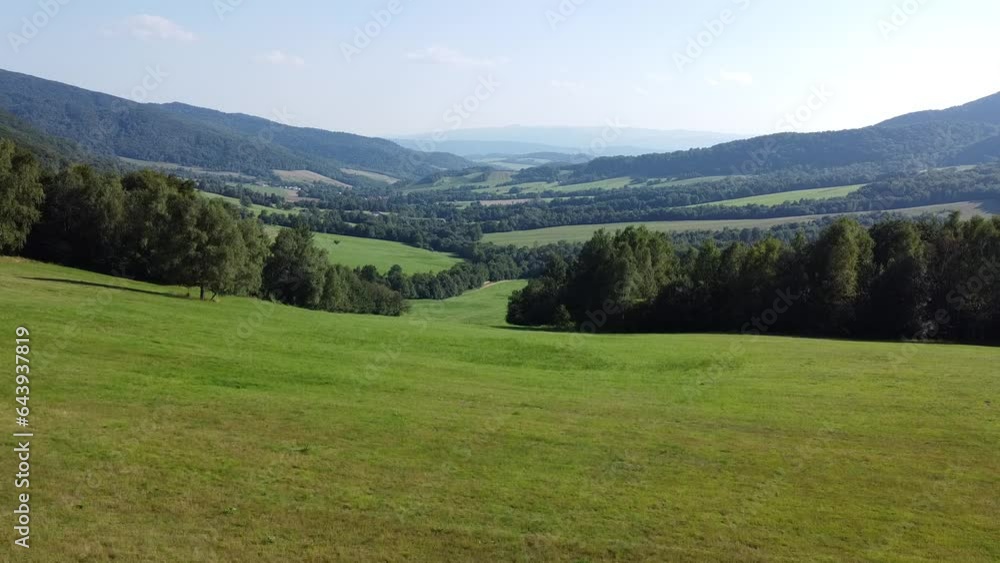 View of a vast, grassy and tree-covered mountain valley on a sunny day. Shot from a drone going up. View of a vast, grassy and tree-covered mountain valley on a sunny day. Shot from a drone going up.