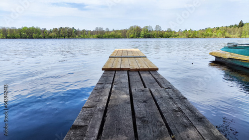 A wooden pier made of old planks on the water of a lake or river and a forest far in the background. Beautiful, calm, natural landscape on a summer, spring or autumn day