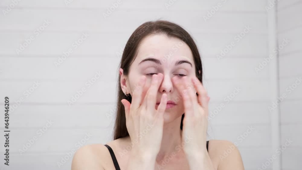 Woman does natural makeup applying concealer on flawless fresh skin by fingertips. Girl looking at mirror. Conceal bruises and skin irregularities. Beauty face. Copy space. Morning visage preparation. Woman does natural makeup applying concealer on flawless fresh skin by fingertips. Girl looking at mirror. Conceal bruises and skin irregularities. Beauty face. Copy space. Morning visage preparation.