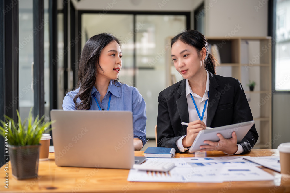 Two focused Asian businesswomen or female accountants are discussing work, examining financial data Two focused Asian businesswomen or female accountants are discussing work, examining financial data