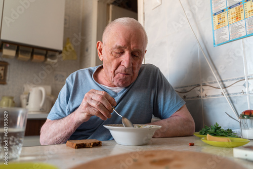 Elderly senior man eating soup with bread and green onion at home in the kitchen. Happy retirement, simple whole food.
