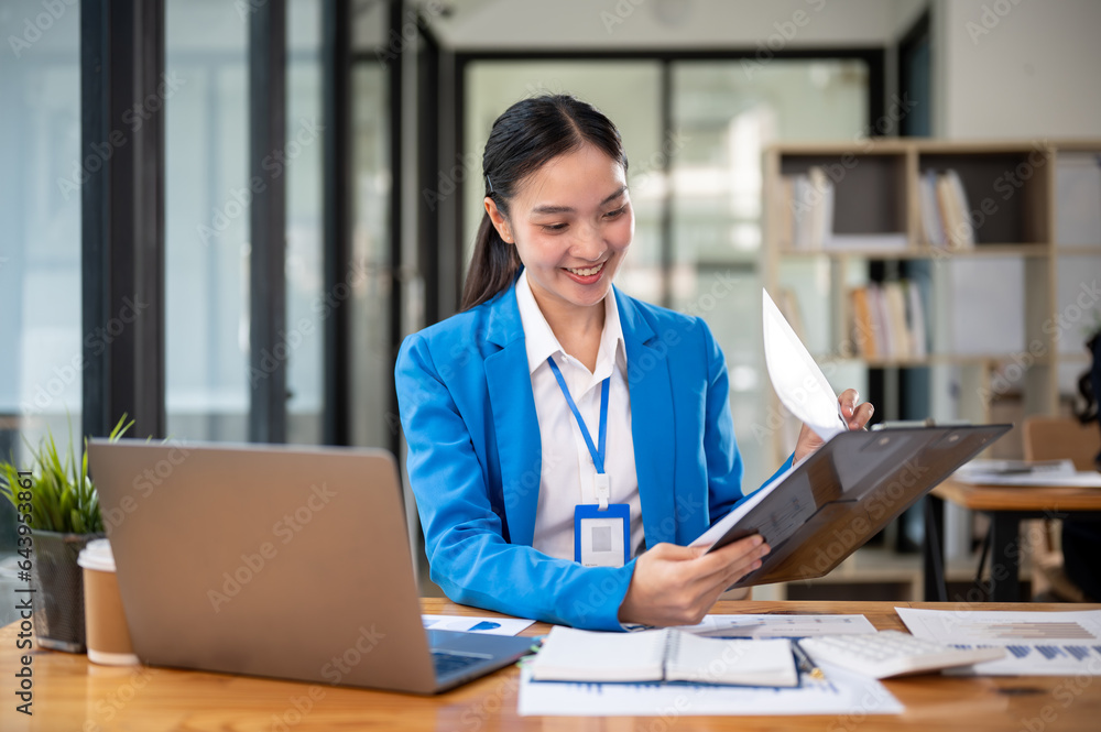 A professional Asian businesswoman or female banker is examining business documents at her desk. A professional Asian businesswoman or female banker is examining business documents at her desk.