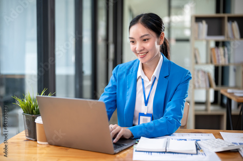 A confident Asian businesswoman is managing her work on her laptop at her desk.