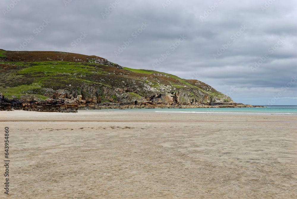 Looking north to the headland on one end of Garry Beach on the Isle of Lewis on an overcast day in June, with the flat empty beach at low tide.