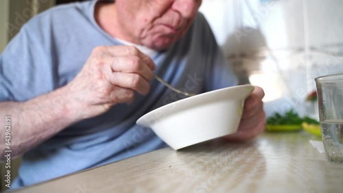 Elderly senior man eating soup with bread and green onion at home in the kitchen. Happy retirement, simple whole food.