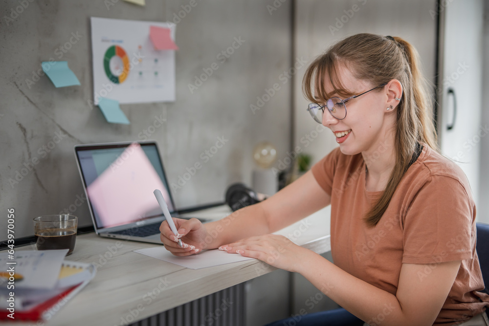 Young female student sitting at table and writing notes, learning at home concept Young female student sitting at table and writing notes, learning at home concept
