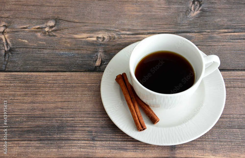 white cup of coffee with cinnamon sticks on the saucer on wooden table copy space  