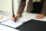Closeup view of businesswoman signing contract, reviewing documents on office desk